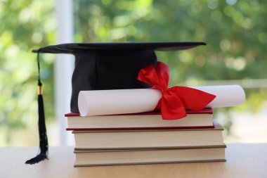 Mezuniyet şapkası, ahşap masada yığınla kitap ve diploma bulanık yeşil arka plan, yakın plan