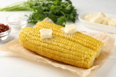 Beyaz ahşap masada tereyağlı, baharatlı ve maydanozlu haşlanmış mısır koçanları.