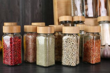 Gri ahşap masada cam kavanozlarda farklı baharatlar, yakın plan.