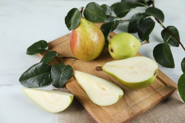 Taze armutlar ve yeşil yapraklar beyaz mermer masada, yakın plan.