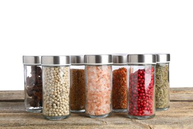 Ahşap masadaki cam kavanozlarda beyaz arka plana karşı çok farklı aromatik baharatlar.