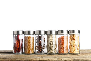 Ahşap masadaki cam kavanozlarda beyaz arka plana karşı çok farklı aromatik baharatlar.