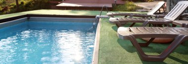 Empty sun loungers on artificial grass near outdoor swimming pool