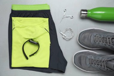 Sportswear, shoes, earphones and water bottle on grey background, flat lay