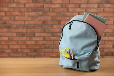 Açık mavi sırt çantası ve ahşap masanın üzerinde kırmızı tuğla duvara karşı farklı kırtasiye malzemesi. Metin için boşluk