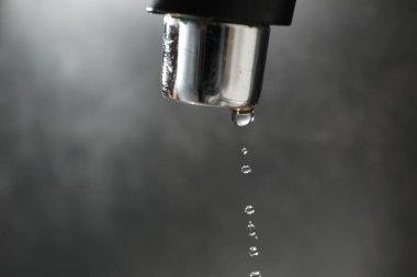 Water dripping down from faucet on grey background, closeup. Space for text