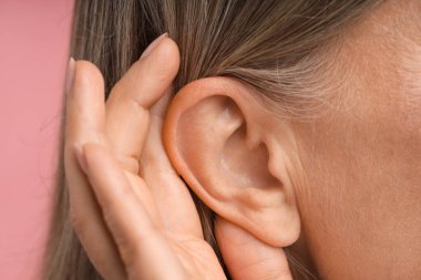 Ses geliyor. Üst düzey kadın pembe arka planda el ele hareketler gösteriyor, yakın plan.