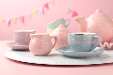 Ahşap masadaki çocuklar için güzel seramik çay seti. Pembe arka planda, parti bayraklarıyla, yakın plan.