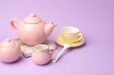 Beautiful ceramic tea set for children on violet background, closeup. Space for text