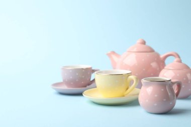 Beautiful ceramic tea set for children on light blue background, closeup. Space for text