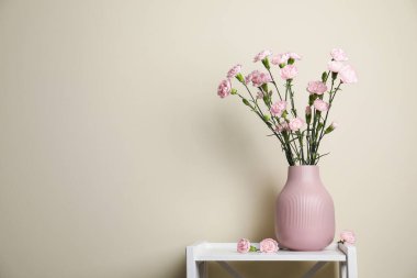 Beautiful carnation flowers in vase on white stand near beige wall indoors, space for text