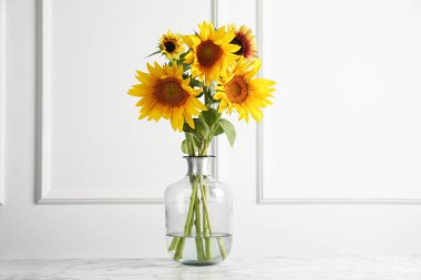 Beautiful sunflowers in glass vase on white marble table indoors