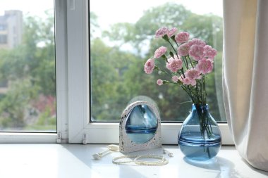Beautiful carnation flowers in vase, mirror, jewellery and face roller near window indoors