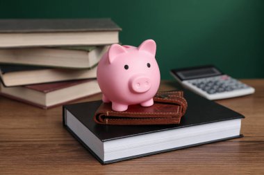 Piggy bank, wallet, calculator and books on wooden table against green background, selective focus