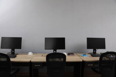 Ofisin içini aç. Açık gri duvarın yanında bilgisayarları olan modern işyerleri