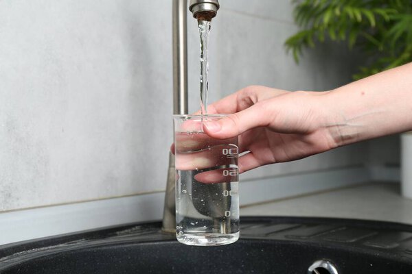 Женщина берет образец воды из крана в помещении, крупным планом. Проверка качества