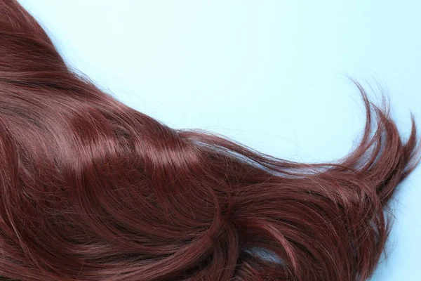 Lock of brown hair on light blue background, closeup. Space for text