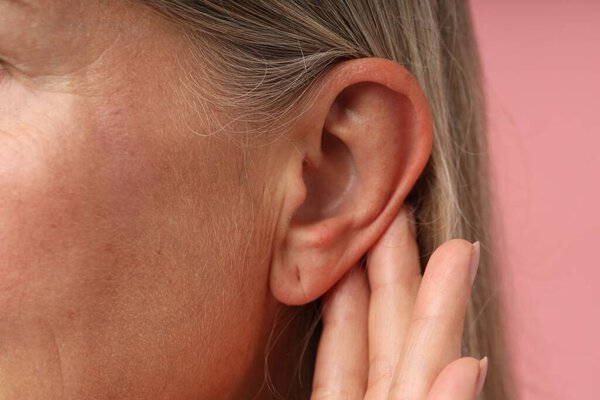 Звук. Старшая женщина прикасается к уху на розовом фоне, крупным планом