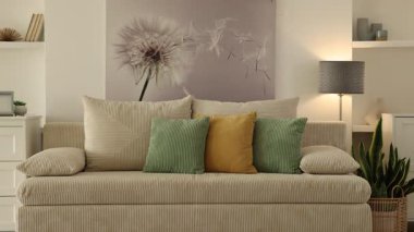 Lambası, çiçekleri ve kanepesi olan şık bir oturma odası. Kamera sağa hareket ediyor