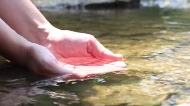 Su kavramını sakla. Nehirden temiz suyu eline alan kadın, yakın plan.