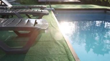 Empty sun loungers on artificial grass near outdoor swimming pool