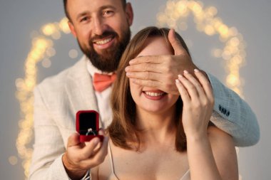 Nişan yüzüklü bir adam, açık gri arka planda, bulanık ışıklı, bokeh efektli kız arkadaşına evlenme teklif ediyor.