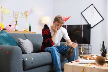 İçki şişesi olan bir adam partiden sonra dağınık bir odada kanepede akşamdan kalma.