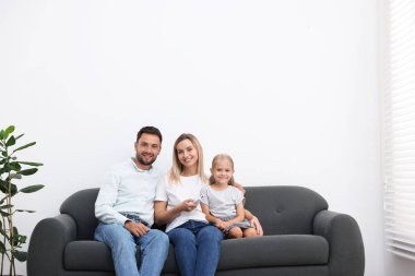 Mutlu aile evdeki kanepede klimayı uzaktan kumandayla kontrol ediyor. Metin için boşluk