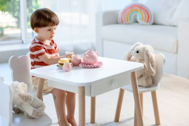 Şirin küçük çocuk içeride oyuncaklarıyla çay partisi yapıyor.