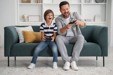 Evde kanepede video oyunu oynayan kontrolörlü baba ve oğul.