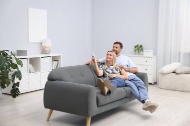 Evdeki kanepede klima kontrol etmek için uzaktan kumanda kullanan çift. Metin için boşluk