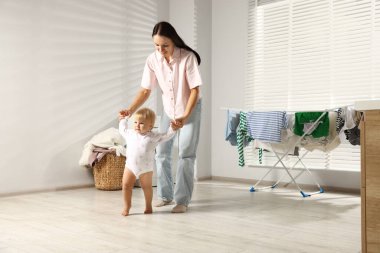 Gülümseyen anne kızına destek olurken o evde yürümeyi öğreniyor.