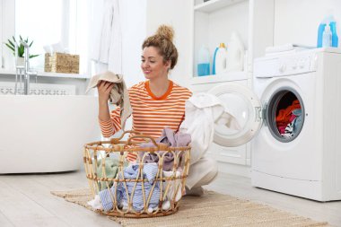 Çamaşır makinesinin yanında çamaşırları olan mutlu kadın.