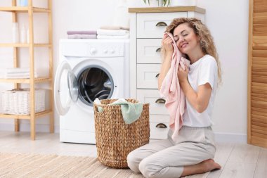 Çamaşır makinesinin yanında temiz çamaşırları olan bir kadın.