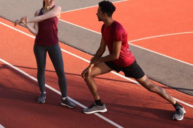 Spor giyimli bir çift stadyumda koşmadan önce ısınma egzersizleri yapıyor.