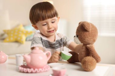 Oyuncak ayısıyla evde çay partisi yapan sevimli küçük çocuk.