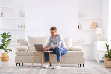 Evde kanepede dizüstü bilgisayar kullanan genç adam