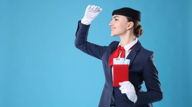 Pasaportu ve açık mavi arka planda biletleri olan gülümseyen hostes. Metin için boşluk