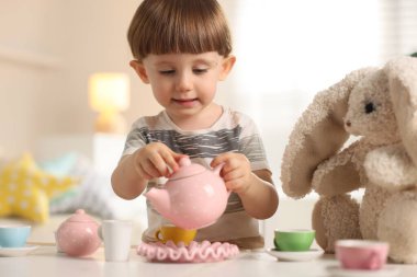 Oyuncak tavşancığıyla evde çay partisi yapan şirin bir çocuk.