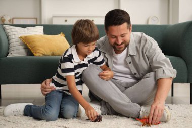Baba oğul evde dinozor oyuncaklarıyla oynuyorlar.