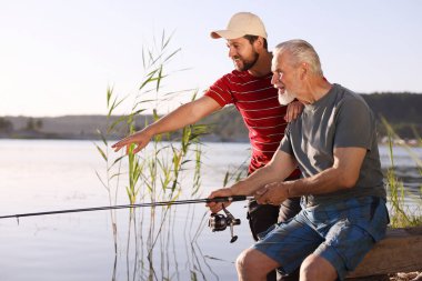 Yaşlı babası ve mutlu oğlu birlikte nehir kenarında balık tutuyorlar.