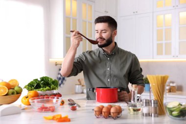 Gülümseyen adam mutfakta yemek yaptıktan sonra yemeği tadıyor.