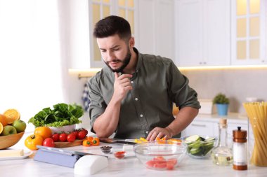 Mutfakta yemek pişirirken tabletten yemek tarifine bakan genç bir adam.