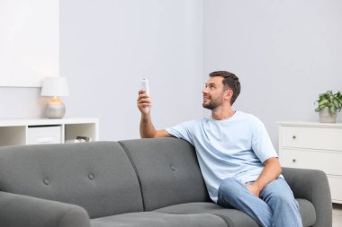 Evdeki kanepede uzaktan kumandayla klima kullanan bir adam. Metin için boşluk