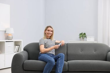 Evdeki kanepede klimalı uzaktan kumandalı bir kadın. Metin için boşluk