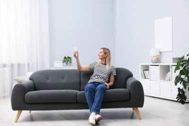 Evdeki koltukta uzaktan kumandayla klima kullanan bir kadın.