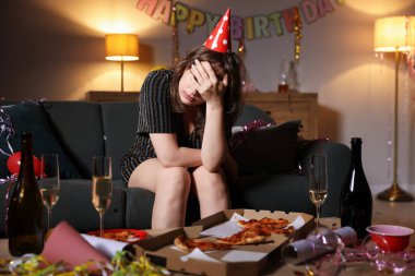 Akşamdan kalma bir kadın partiden sonra dağınık bir odada kanepede yatıyor.