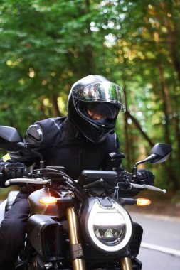 Kasklı genç adam modern motosikleti açık havada kullanıyor.