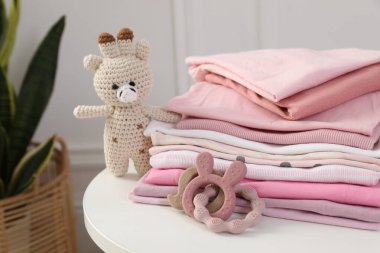 İçerideki beyaz masada temiz bebek kıyafetleri ve oyuncaklar yığını, yakın plan.