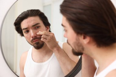 Evinde aynanın yanında sivilce sorunu olan genç bir adam var.